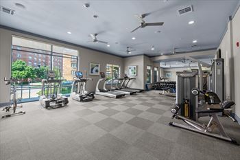 A spacious gym with a variety of equipment and a view of a cityscape outside the window.